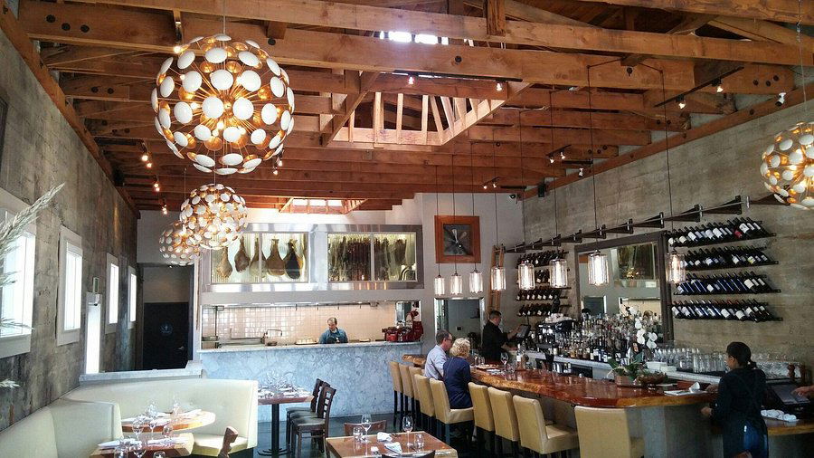 An elegantly set long dining table with candlelight, wine glasses, floral centerpieces, and place settings in a warm, intimate restaurant interior.