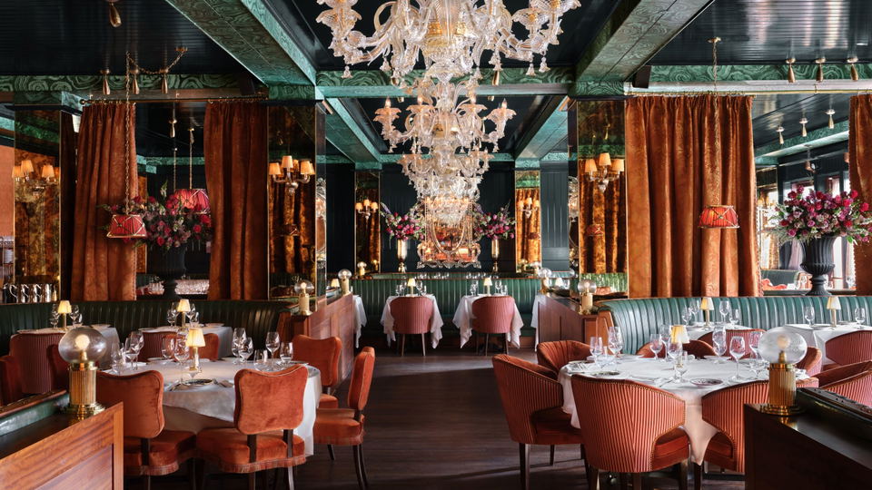 Elegant dining room with chandeliers, velvet chairs, and set tables