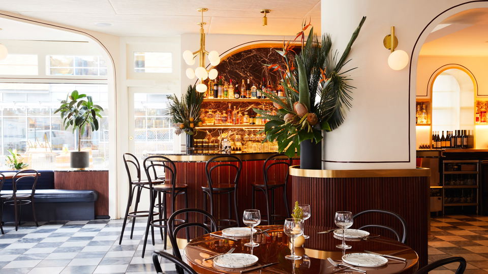 A bright, elegantly designed restaurant dining room featuring black bentwood chairs, warm wood tables, a black-and-white marble checkerboard floor,