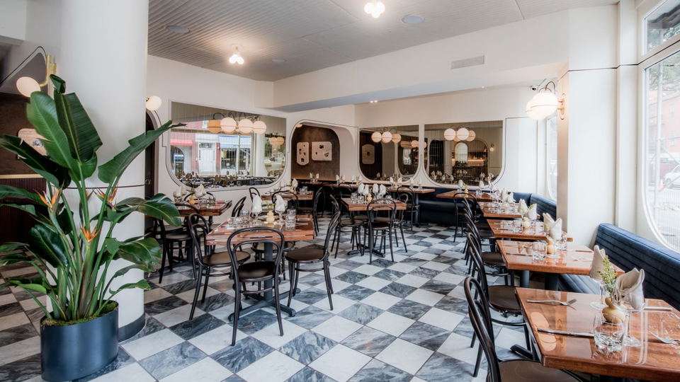 A warmly lit dining room at Don Angie in the West Village, with bentwood chairs, checkered marble floors, and globe pendant lights.