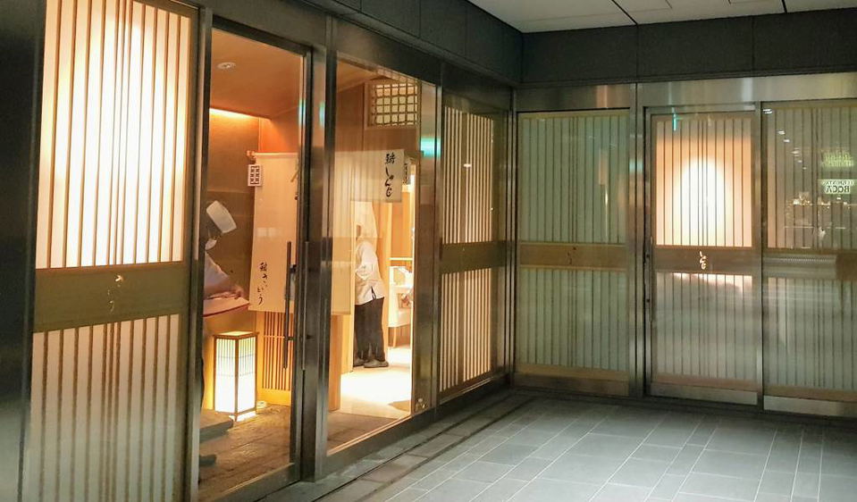 A covered passageway leading to a building entrance, with a small security booth and a 'bicycle parking' sign in Japanese.