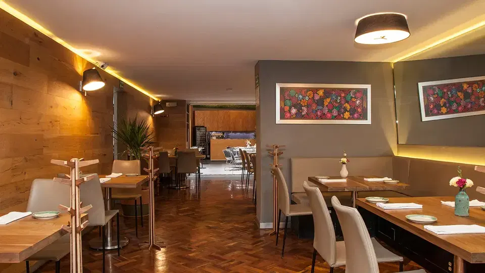 A warmly lit, intimate restaurant dining room with wood parquet floors, upholstered banquette seating, set tables with glassware and napkins, pendant