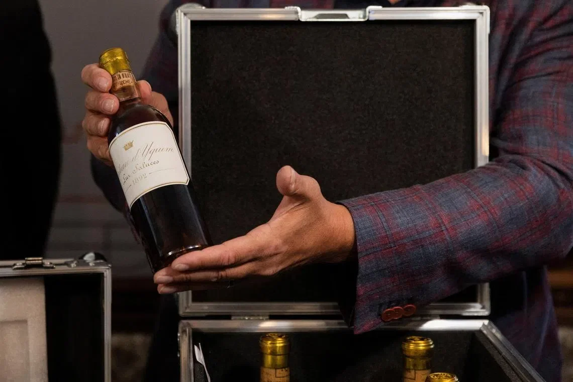 A person holds a bottle of 1892 Château d'Yquem, with a gold foil top and a white label featuring a crown and text, over an open case.