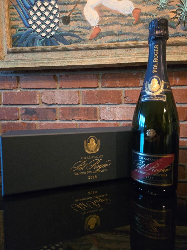Bottle of 2018 Pol Roger Cuvée Sir Winston Churchill Champagne beside its black and gold presentation gift box on a reflective dark surface.