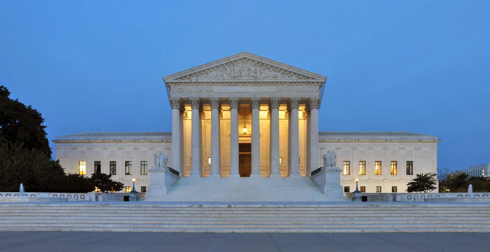 The Supreme Court building at dusk, with its illuminated columns and grand staircase, under a clear blue sky.