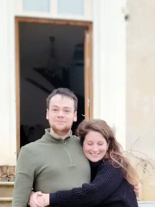 Hugo Mathurin and Talloulah Dubourg at Domaine de Cassiopée, embracing on the steps of a rustic French country house.