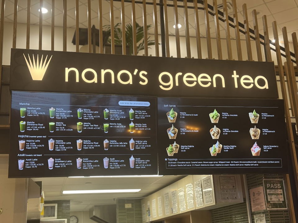 A menu board for Nana's Green Tea, featuring various matcha, hojicha, and azuki drinks, along with soft serve options and toppings.