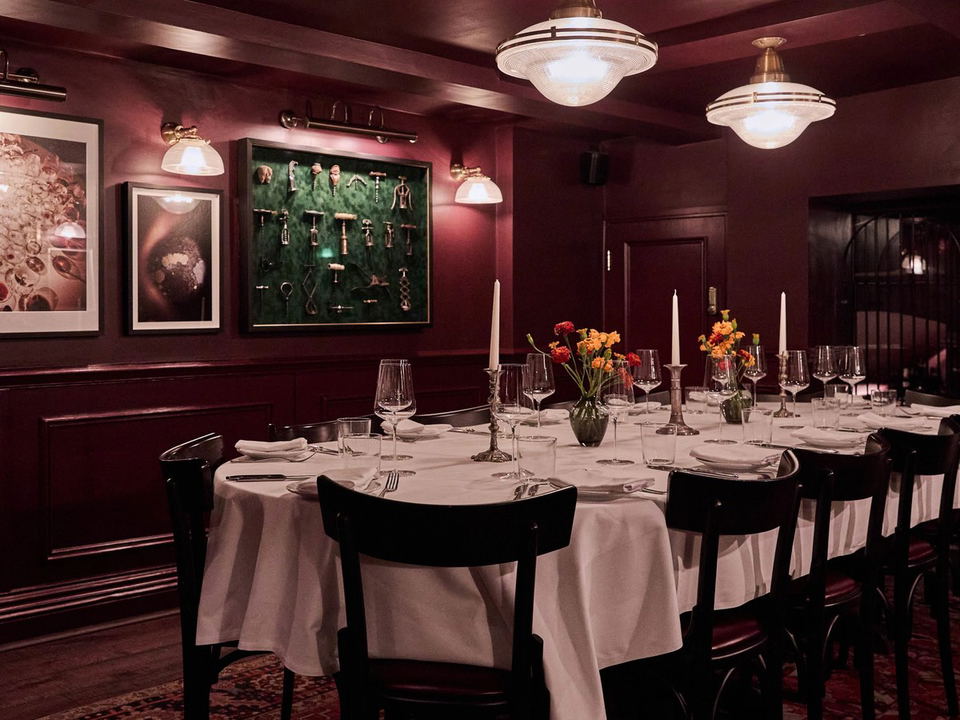 An intimate private dining room at Noble Rot Mayfair, featuring deep crimson walls, dark wood paneling, and a long table set with white tablecloths,