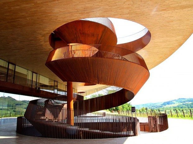 A dramatic, weathered Corten steel spiral staircase and ramp structure at the Antinori nel Chianti Classico winery, with rolling Chianti hills.