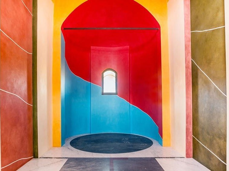 A vibrant interior of the Cappella delle Brunate, featuring bold Sol LeWitt and David Tremlett color-field fresco murals in red, blue, yellow.