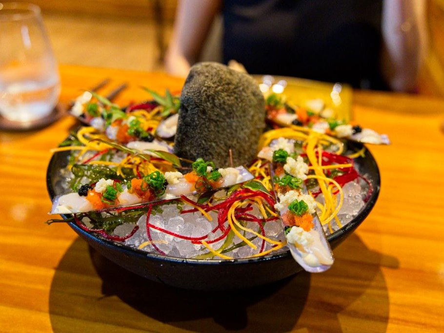 Maido's razor clams, a Nikkei masterpiece, are artfully presented with vibrant garnishes on a bed of ice.