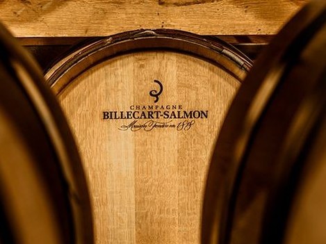 A close-up view of oak wine barrels, with the central barrel clearly displaying the "Champagne Billecart-Salmon" brand name.