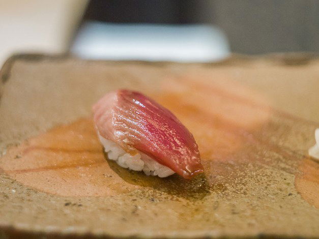 A single piece of nigiri sushi rests on a rustic plate, a glimpse into the omakase experience at Sushi Saito.