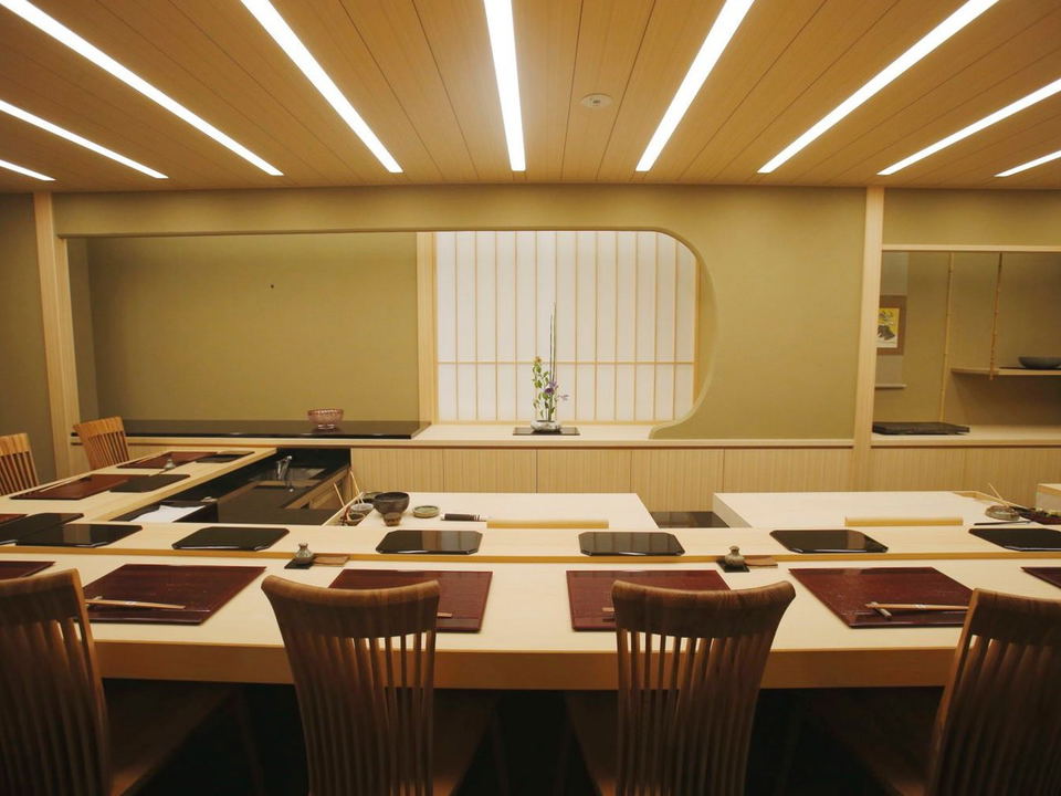 A pristine Japanese omakase counter interior with shoji screen backdrop and ikebana arrangement.