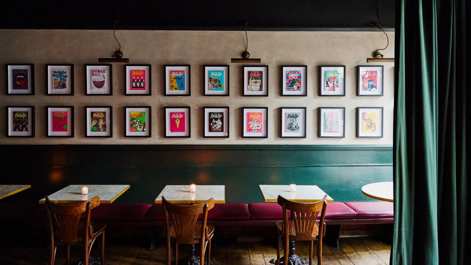 Magazine covers lining the wall at Noble Rot, above a banquette with red upholstery, marble-topped tables, and wooden chairs.