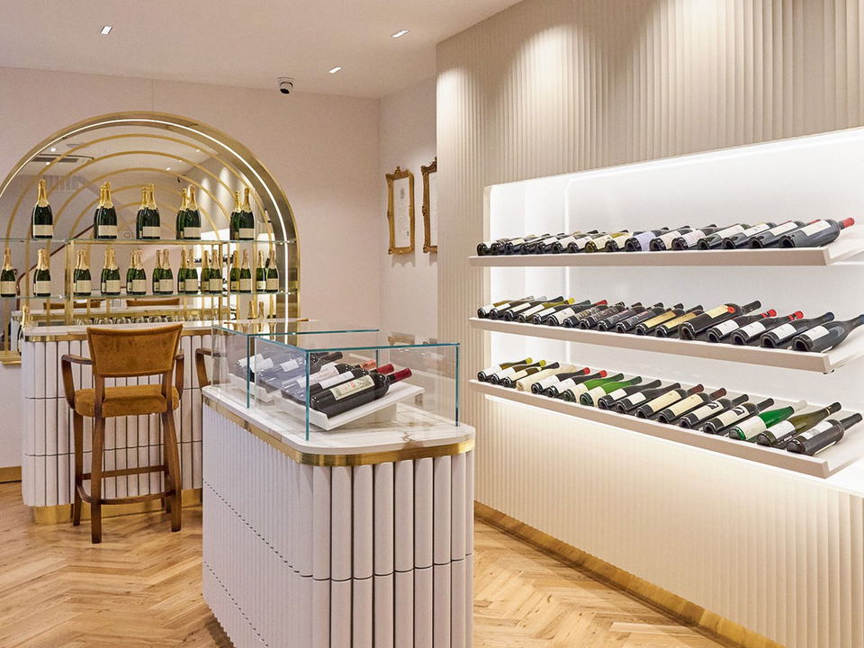 An elegant wine shop interior with illuminated shelves of wine bottles, a marble display counter, and a gold arched champagne display.