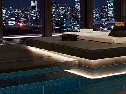 Aman Tokyo's spa pool area at night, with a treatment platform and floor-to-ceiling windows overlooking the Tokyo skyline and Tokyo Tower.