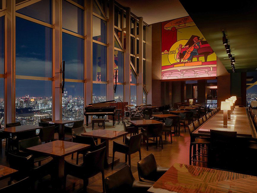 High-rise restaurant interior with city view, piano, and illuminated tables.