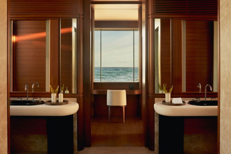 A luxury bathroom interior at Amanvari with twin black pedestal sinks, each with a chrome faucet, flanking a central window overlooking the Sea of