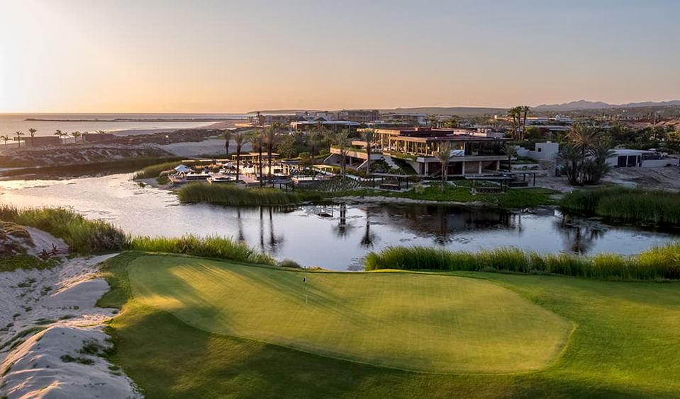 Costa Palmas Peninsula View: golf course, luxury residences, and Sea of Cortés shoreline at sunset.