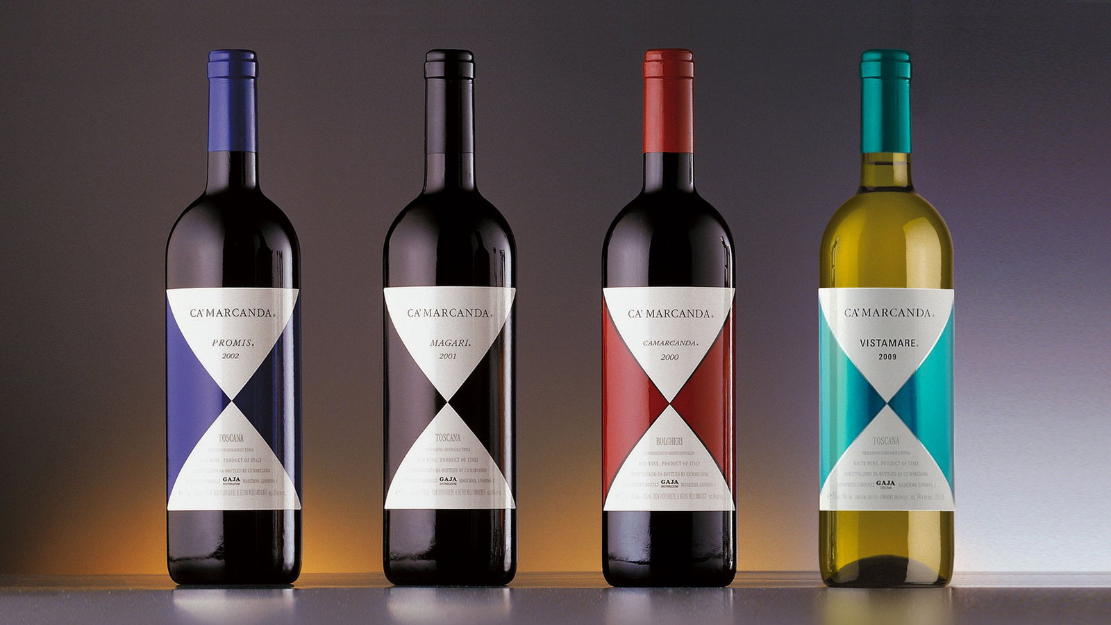 Four Ca'Marcanda wine bottles by Gaja displayed in a row: Promis 2002 (blue foil), Magari 2001 (black foil), Camarcanda 2000 (red foil), and Vistamare 2009 (teal foil), each with a distinctive diamond-pattern label.