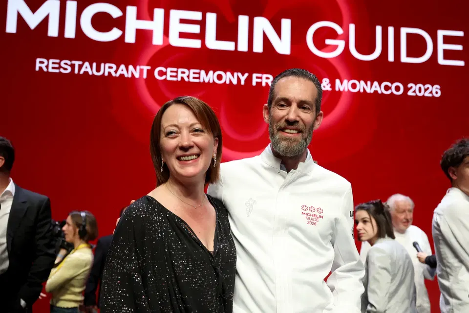 Two people smiling at Michelin Guide 2026 restaurant ceremony in front of red backdrop with white Michelin branding and text