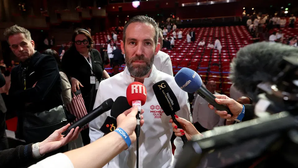 Chef in white Michelin Guide 2026 jacket interviewed by multiple microphones at auditorium event