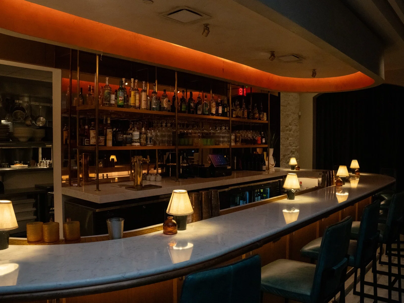 An interior shot of Avize in Atlanta, featuring a long, curved bar with several small, illuminated lamps, and shelves stocked with various bottles of