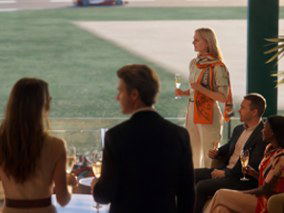 Elegantly dressed guests enjoy champagne in a luxurious open-air hospitality terrace with a direct view of a racing circuit.