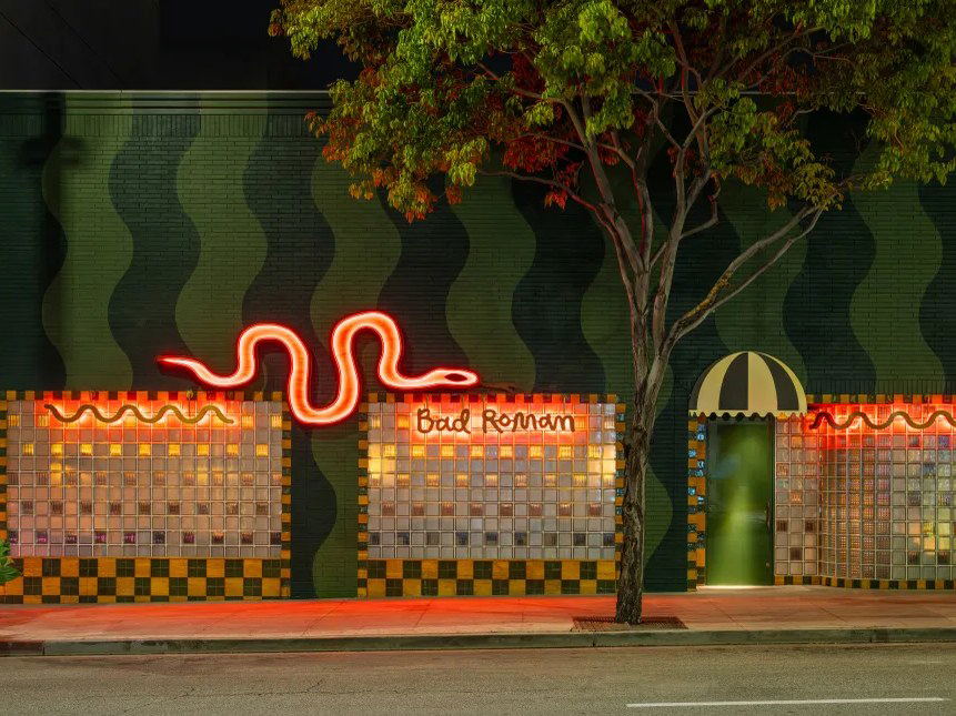 Nighttime exterior facade of Bad Roman Beverly Hills, featuring a neon snake and wavy green walls.