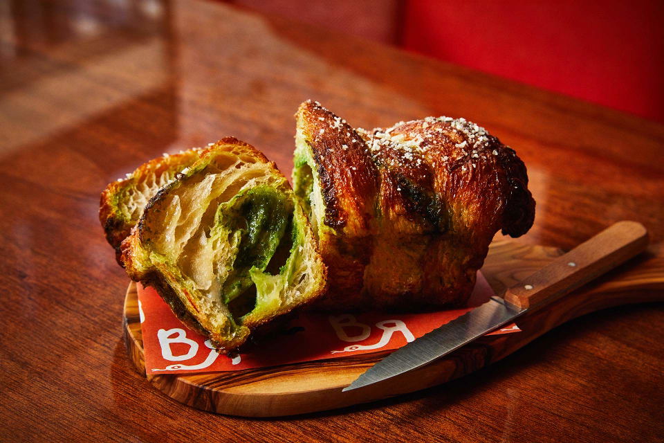 A babka, sliced in half to reveal a vibrant green filling, sits on a small wooden board with a knife beside it.