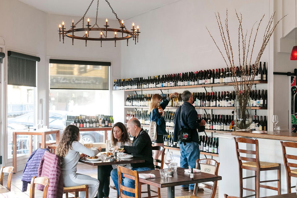 The interior of Kitchen Istanbul, showing diners at tables, shelves of wine bottles, and a large chandelier hanging from the ceiling.