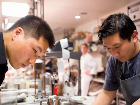 Peter Serpico, a chef, meticulously plates a dish in a bustling professional kitchen, focused on his task.