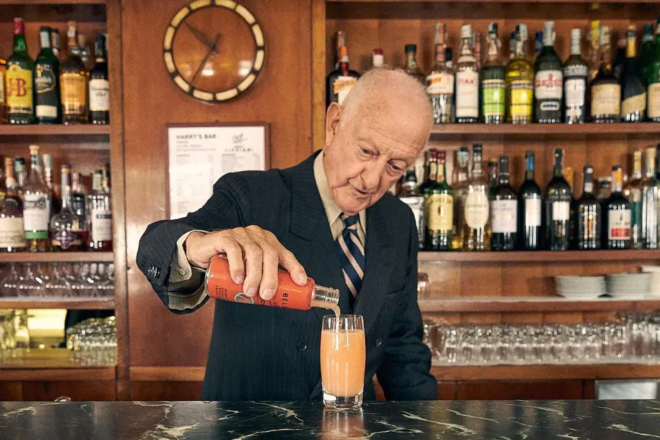 Giuseppe Cipriani, an elderly man in a suit and tie, pours a pink drink from a small bottle into a glass at a bar named Harry's Bar.