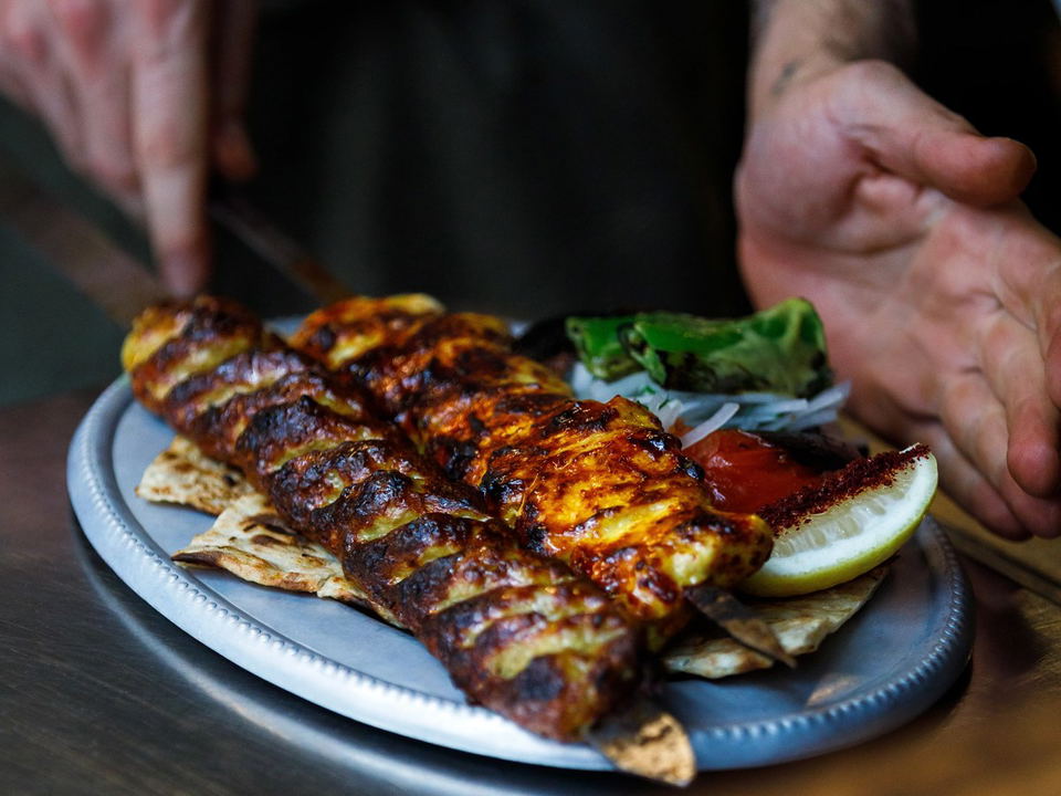 Charcoal-grilled kebab skewers on flatbread with lemon and greens on a dark plate; the source page (Eater) explicitly attests this is 'Kebabs coming o