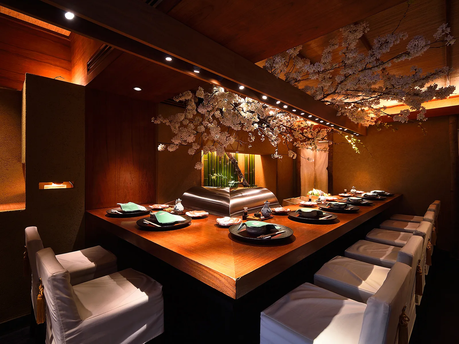 An elegant Japanese restaurant interior with a long wooden table set with dishes and white chairs, adorned with cherry blossoms.