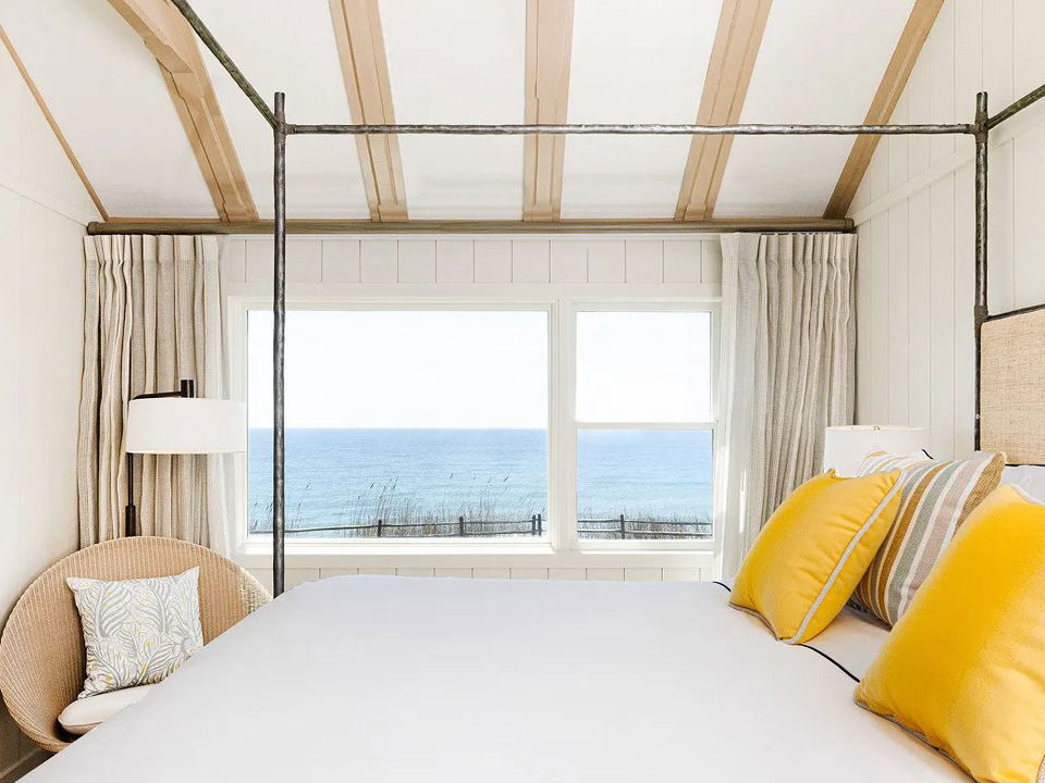 A bright coastal-style hotel guest room at Gurney's Montauk with a four-poster bed, yellow pillows, and an ocean view.