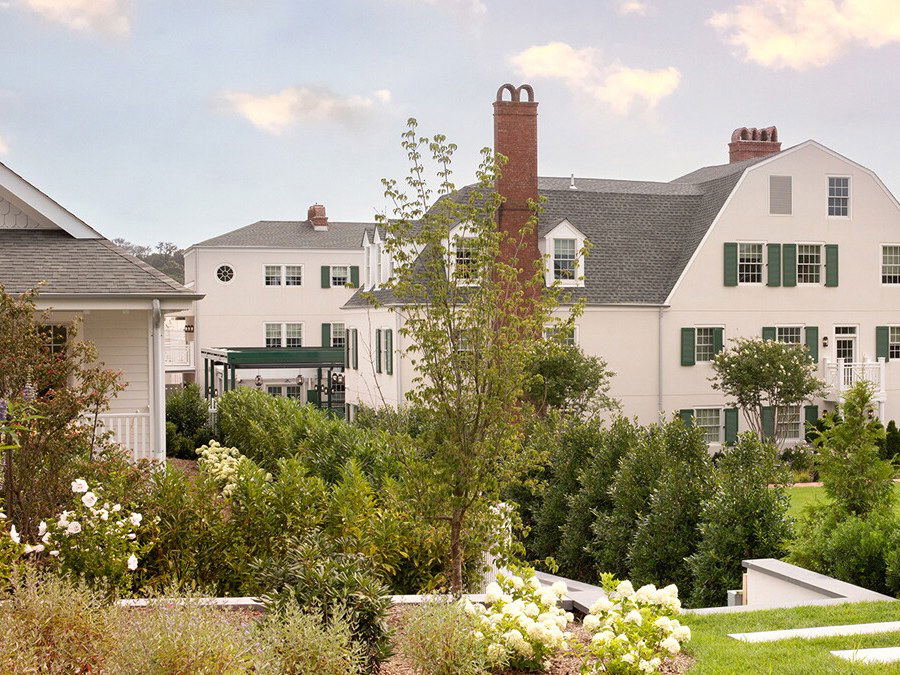 The exterior of Canoe Place Inn in Hampton Bays, a large white building with green shutters, multiple brick chimneys, and a gambrel roof, surrounded