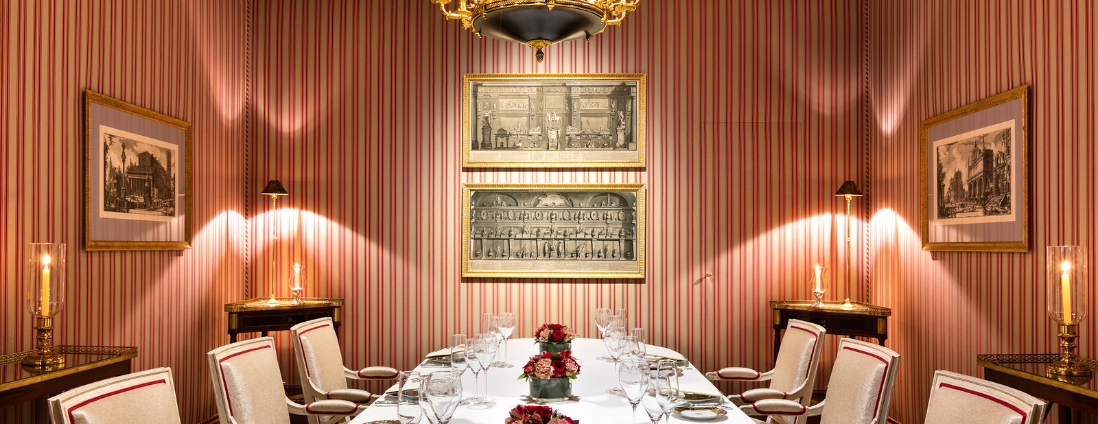 A formal dining room with red and white striped wallpaper, a long table set with white tablecloth, glasses, and floral centerpieces.