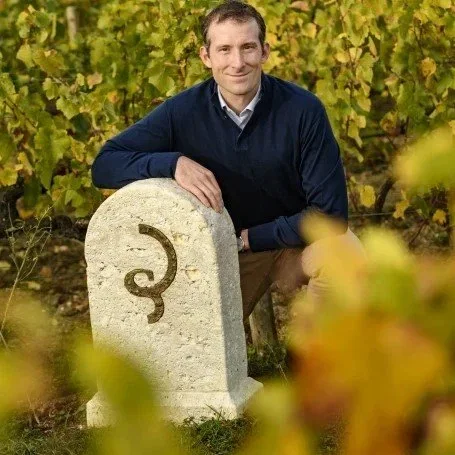 Mathieu Roland-Billecart kneeling beside the Clos Saint-Hilaire vineyard marker stone among autumn vines.