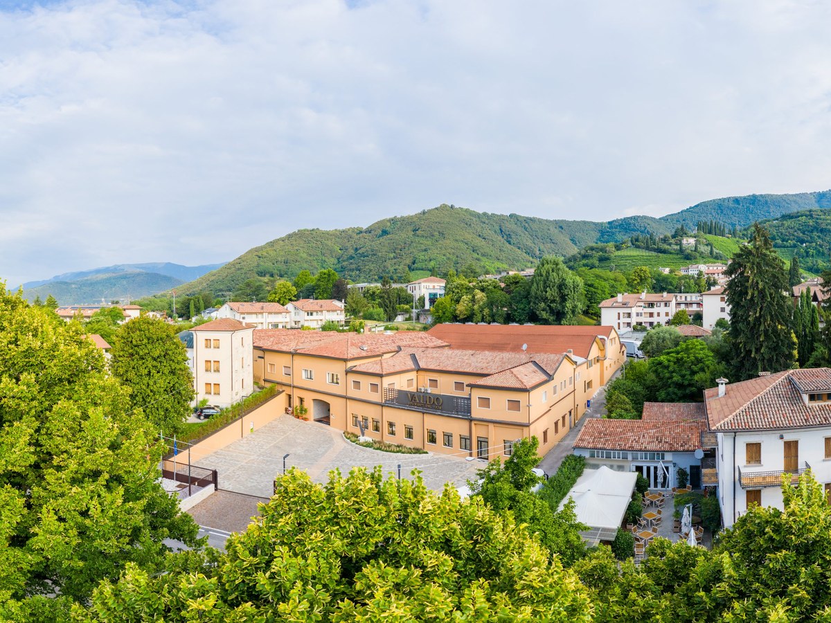 A hillside town with terracotta-roofed buildings and green mountains in the background.
