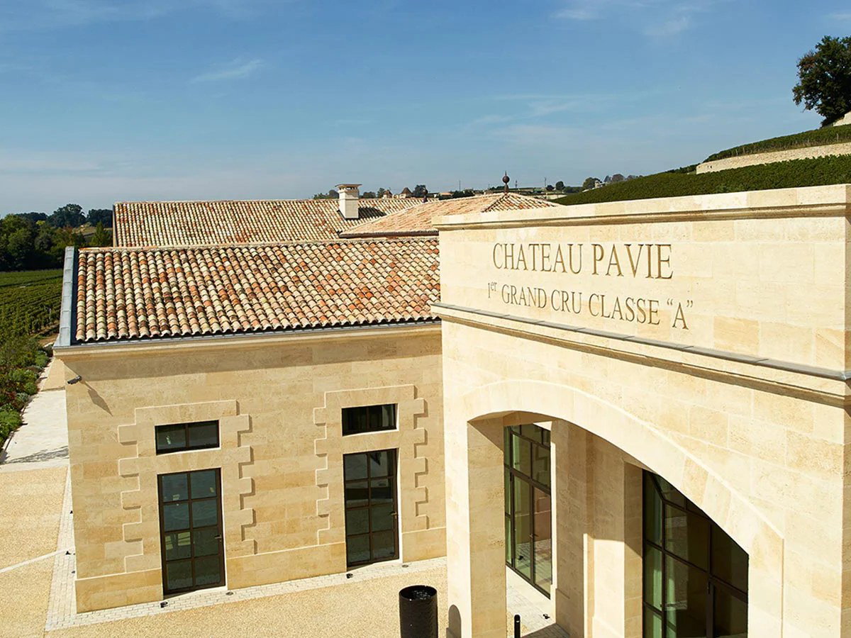 An aerial view of the Château Pavie winery building, made of light-colored stone, with "CHATEAU PAVIE 1ST GRAND CRU CLASSE A" inscribed on its