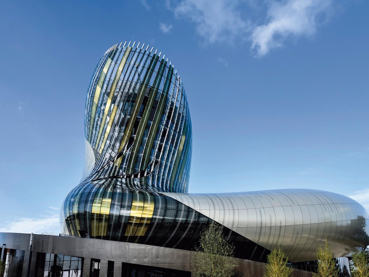 The Cité du Vin building in Bordeaux, with its distinctive fluid, wave-like stainless steel and glass facade under a blue sky.