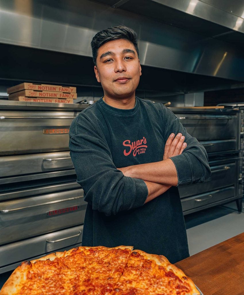Sugar's Hot Pizza (Seaport) showcases a large, freshly baked cheese pizza with a golden crust.