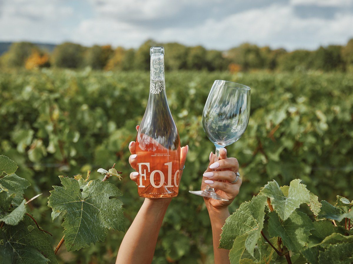 Breaky Bottom Vineyard: Hands hold a bottle of Folo rosé and a wine glass amidst lush vines.