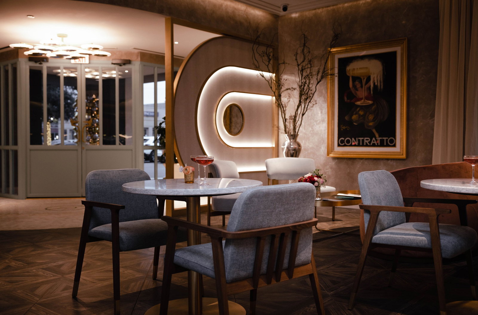 An upscale lounge/bar interior with mid-century modern furniture in blue and pink tones, marble-top tables, and a distinctive illuminated sculptural w