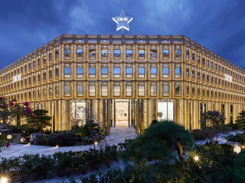 The Dior Bamboo Pavilion in Daikanyama, Tokyo, features a multi-story gold bamboo-lattice facade illuminated at dusk, with a glowing Dior star atop