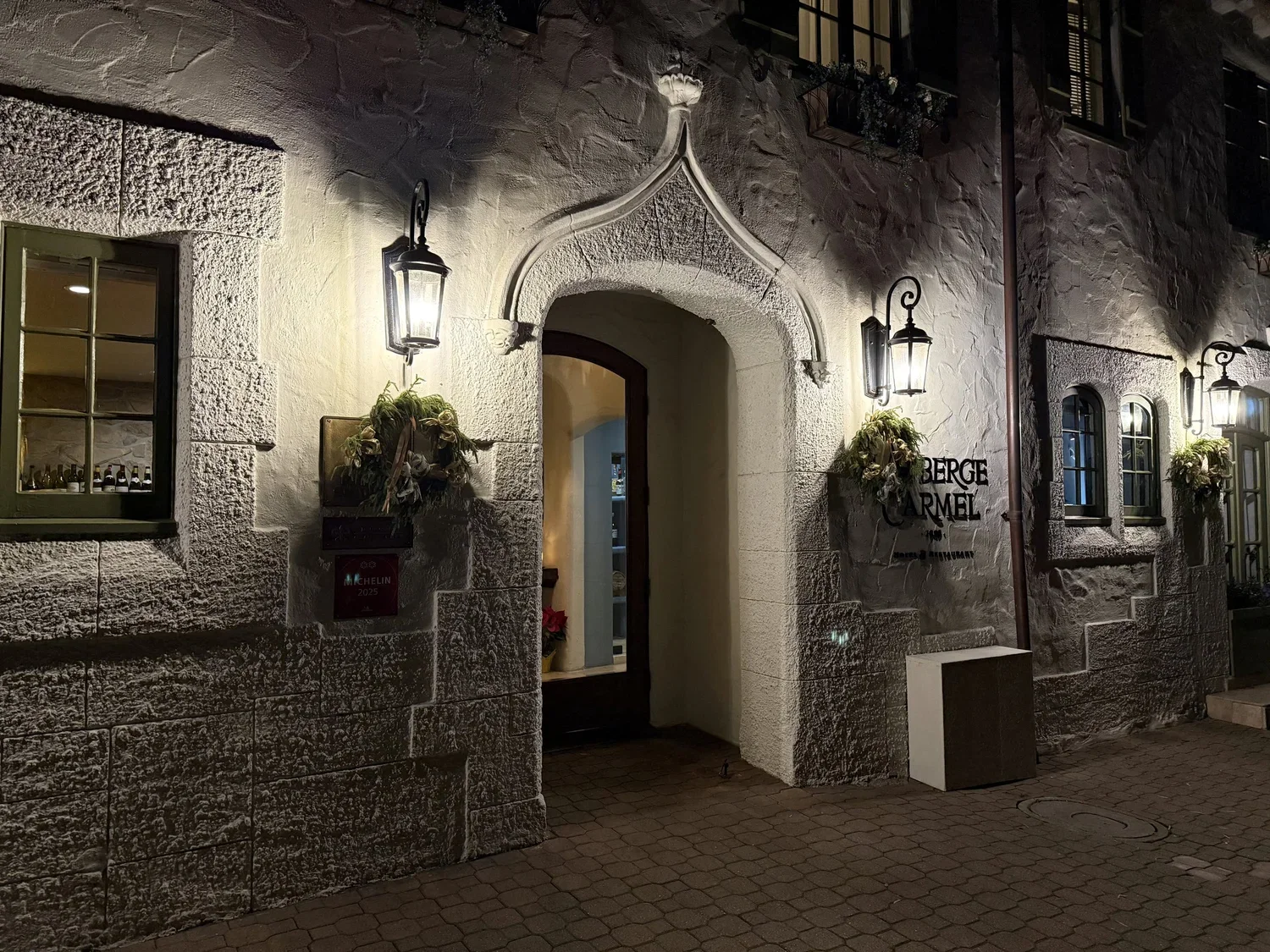 The entrance to Aubergine, a Michelin-starred restaurant, illuminated by lanterns at night, with a Michelin 2025 plaque visible.