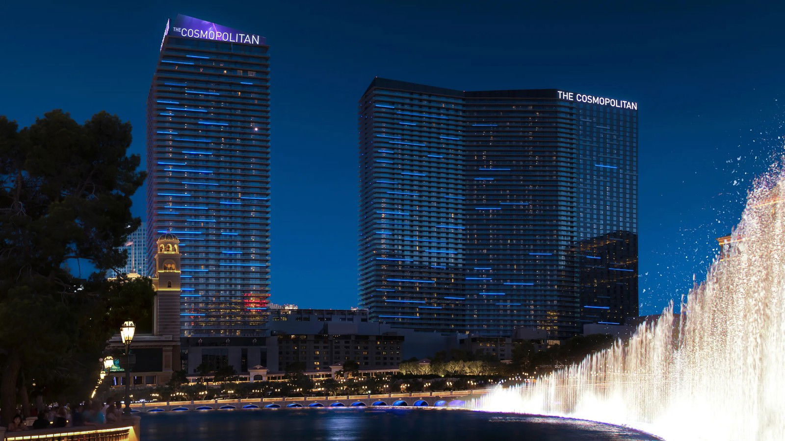 The Cosmopolitan of Las Vegas shines with blue lights as Bellagio fountains dance, a vibrant part of private dining Las Vegas.