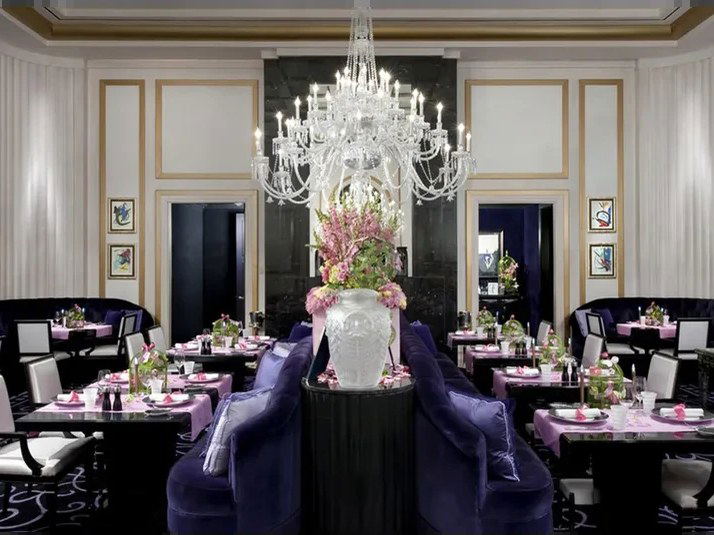 An elegant private dining room at Joël Robuchon, featuring deep purple velvet banquettes, black tables with lavender linens, and a crystal chandelier.